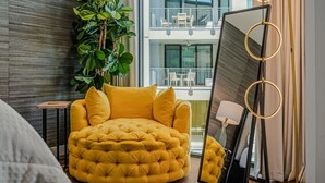 A modern living room with a tufted yellow sofa, a large mirror, and a potted plant.