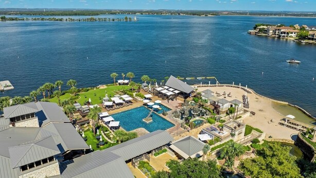 An aerial view of a resort with a large swimming pool, beach area, and multiple buildings with a view of the water.