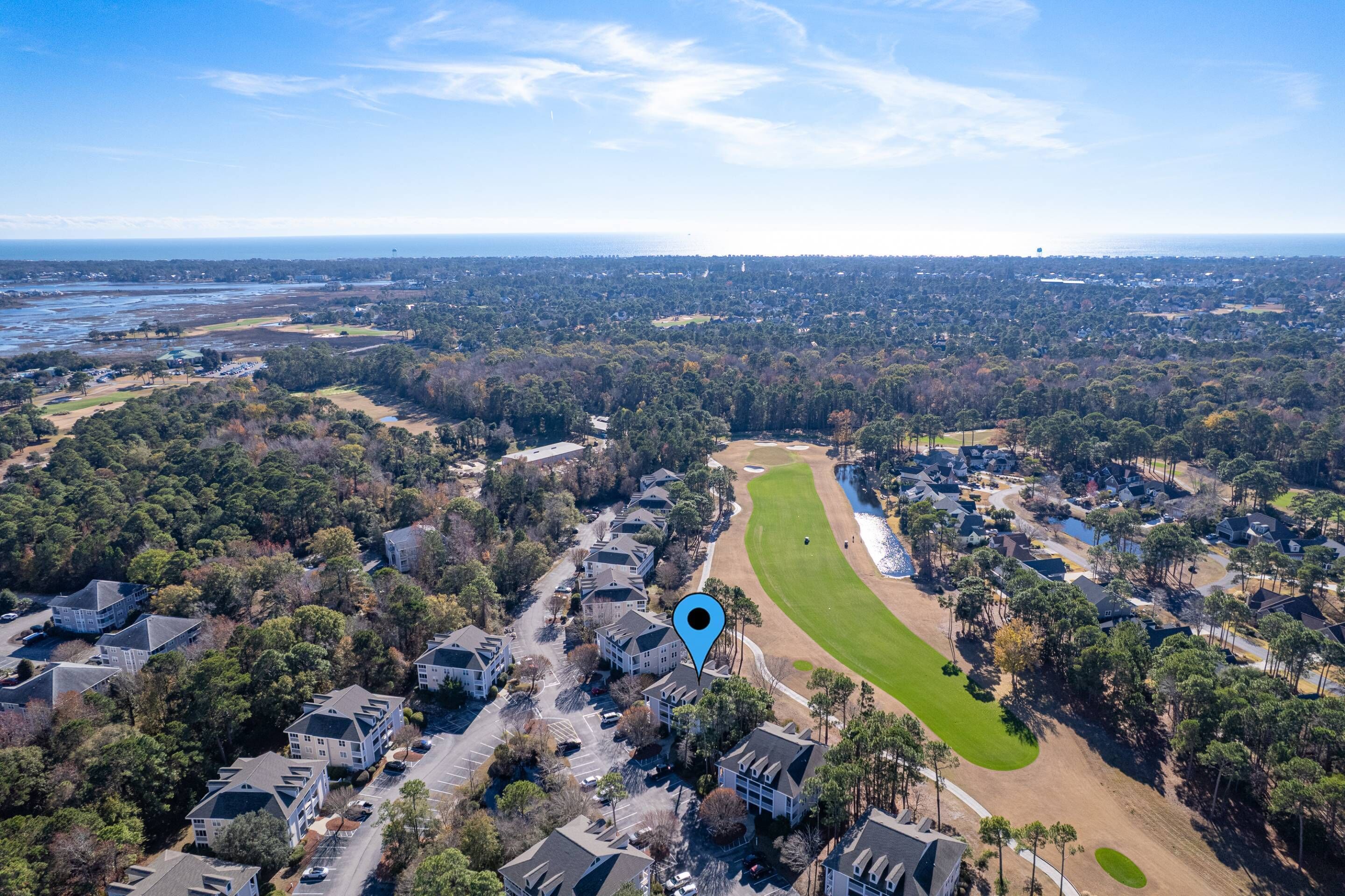 An aerial view of a residential area with houses, a golf course, and a body of water in the distance.