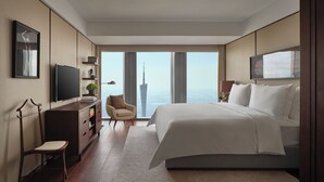 Une chambre d’hôtel moderne, dotée d’un grand lit, d’un bureau, d’une chaise, d’une télévision et offrant une vue sur un immeuble de grande hauteur.