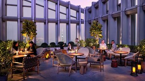 Un espace extérieur aménagé avec des tables et des chaises, entouré de grandes fenêtres et agrémenté de plantes en pot.