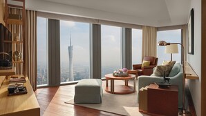 Une chambre d’hôtel moderne avec vue sur la ville, un bureau en bois, un canapé confortable et une table basse ronde.