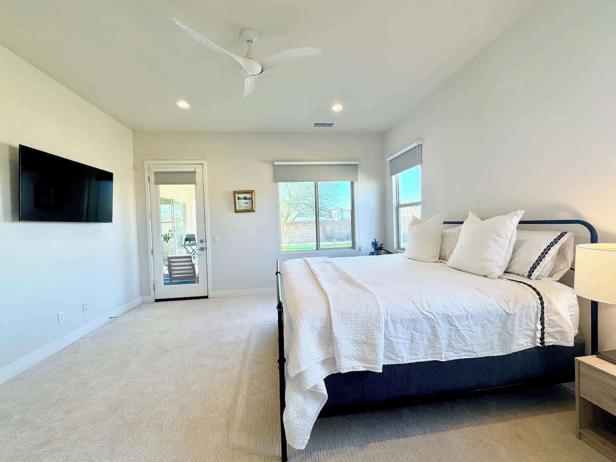 A bedroom with a bed, a TV, a ceiling fan, and a door leading to a balcony.