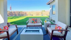 Un patio exterior con un sofá, sillones y una mesa de centro, con vistas a un césped cuidado y una cadena montañosa distante.