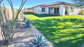 Una casa residencial con techo de tejas, un césped bien cuidado y varias plantas de agave.