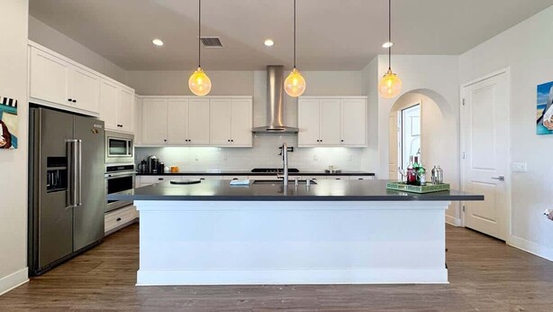 Una cocina moderna con armarios blancos, electrodomésticos de acero inoxidable e iluminación colgante.