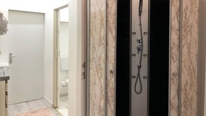Un baño moderno con cabina de ducha, paredes de mármol y un inodoro visible en la habitación contigua.