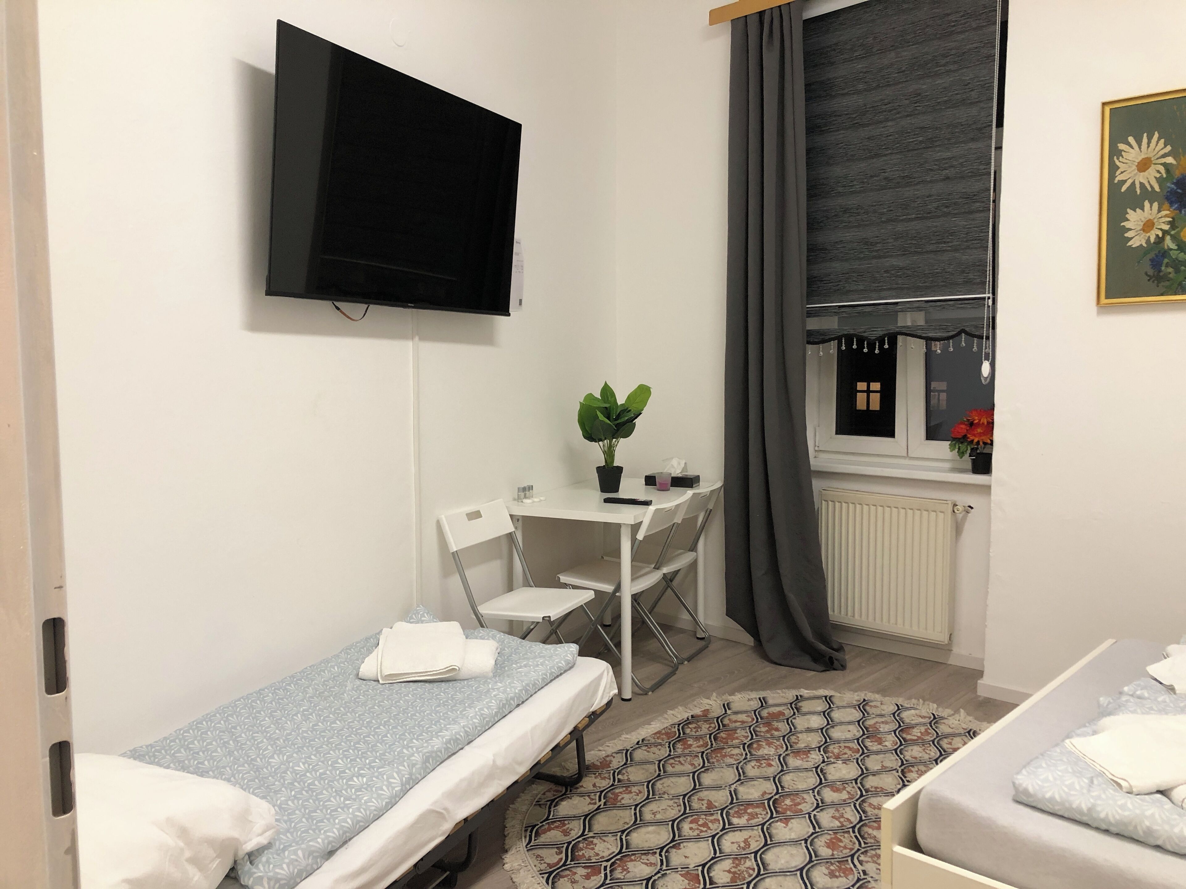 A compact hotel room with a single bed, a small desk with a chair, a television mounted on the wall, and a window with curtains.