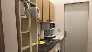 Una cocina compacta con lavadora, microondas y repisas con distintos utensilios de cocina.