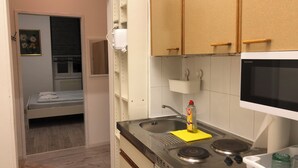 Una cocina compacta con estufa, pileta y microondas. Hay una cama en la habitación contigua.