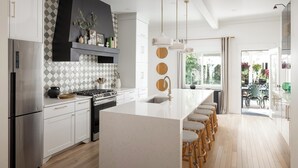 Ett modernt kök med en stor köksö, vitvaror i rostfritt stål och en geometriskt mönstrad väggbeklädnad bakom arbetsbänken.