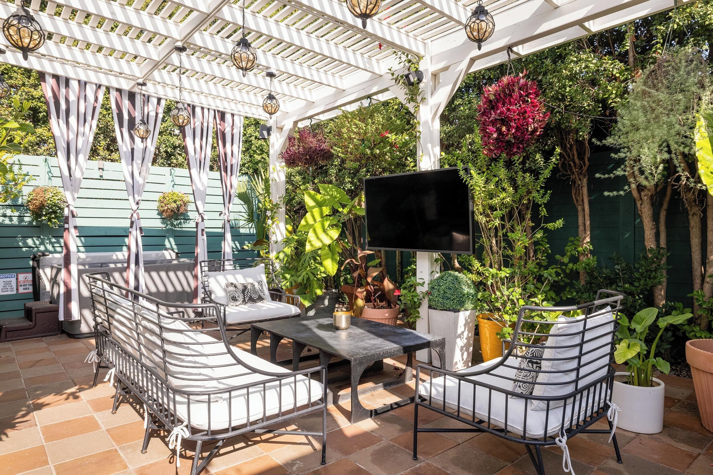 A covered patio with a table and chairs, surrounded by potted plants and a TV screen.