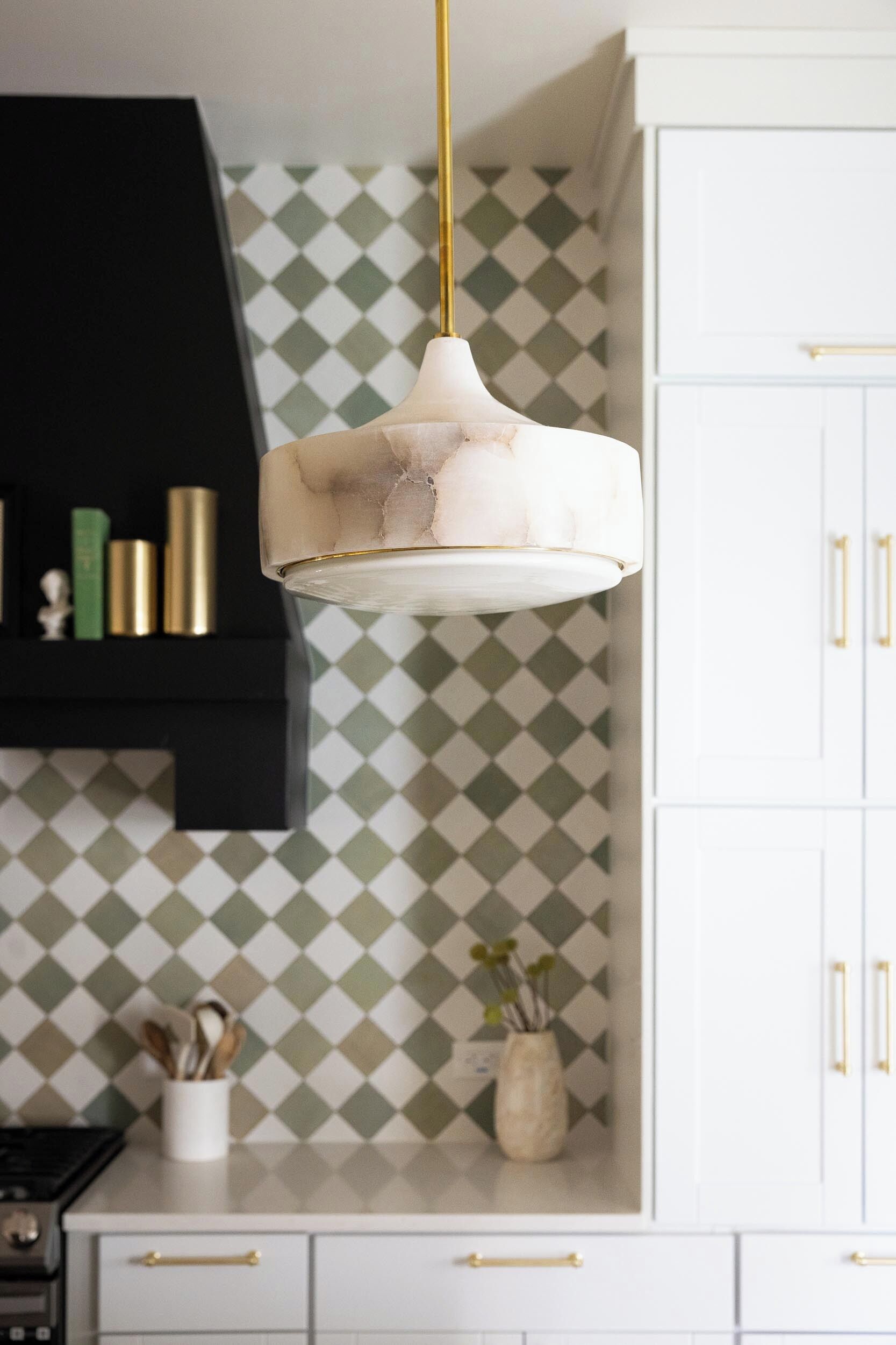 A kitchen with a pendant light, white cabinets, and a patterned backsplash.
