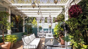 En täckt uteplats med en vit pergola, utomhusmöbler och krukväxter.