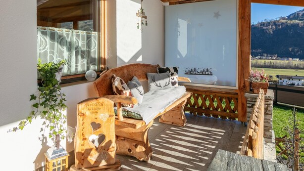 A wooden bench with cushions, a small table, and a decorative wooden piece with heart cutouts. - Lovingly furnished apartement with bbq (Zellberg)