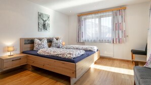 A bedroom with a wooden bed, a nightstand, a lamp, a window with curtains, and a radiator. - Lovingly furnished apartement with bbq (Zellberg)