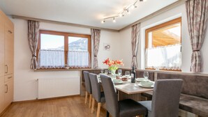 A dining area with a wooden table, grey upholstered chairs, a bench, and a view of the outdoors through large windows. - Lovingly furnished apartement with bbq (Zellberg)