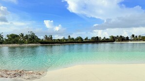 A beach with clear turquoise water, white sand, and palm trees under a partly cloudy sky. - Villa in Vistacana Private Pool Golf Beach (Punta Cana)