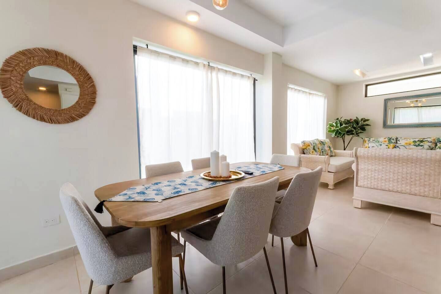 A dining area with a wooden table, grey chairs, and a round mirror on the wall.