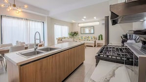 A modern kitchen with a central island, stainless steel appliances, and a dining area with a sofa and table. - Villa in Vistacana Private Pool Golf Beach (Punta Cana)