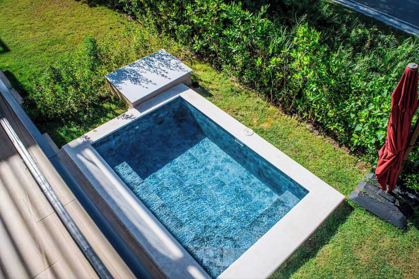 A rectangular swimming pool with a tiled deck, surrounded by well-maintained grass and bushes.