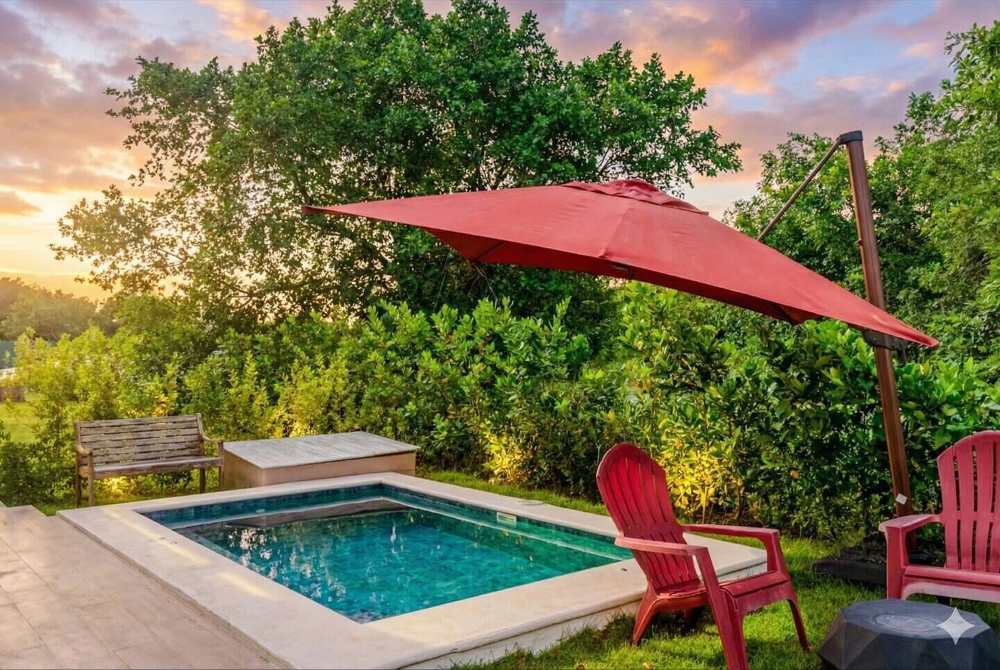 Een rechthoekig zwembad met een rode parasol, omgeven door een stenen terras. Twee rode stoelen en een houten bankje zijn aanwezig.
