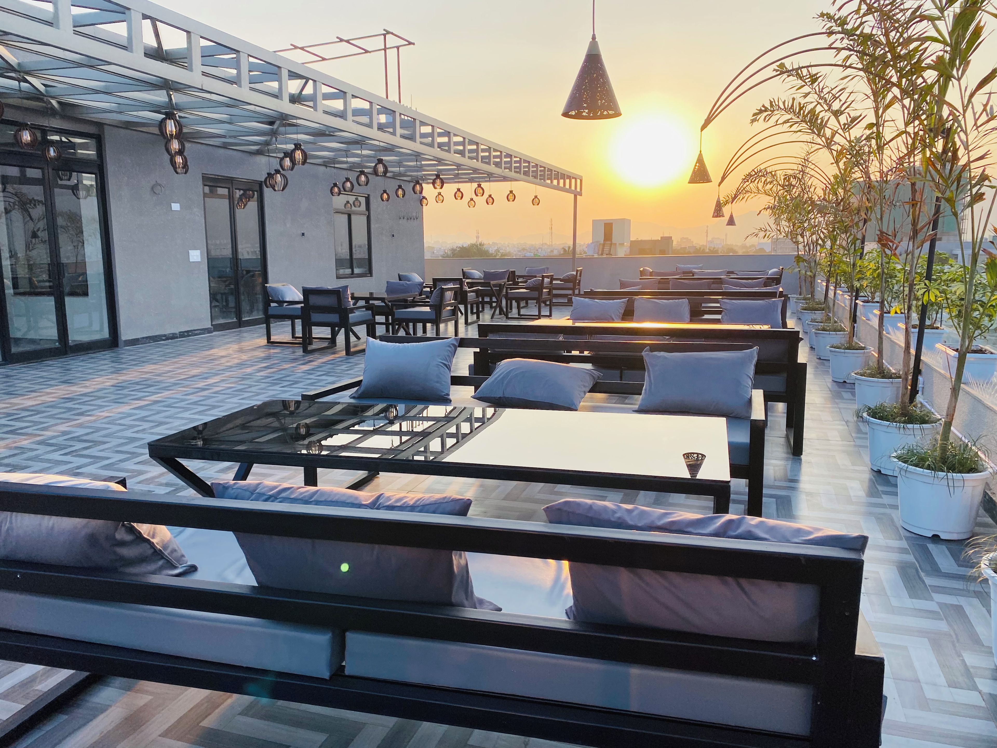 A rooftop terrace with outdoor seating, a glass railing, and hanging pendant lights.
