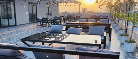 A rooftop terrace with outdoor seating, a glass railing, and hanging pendant lights.