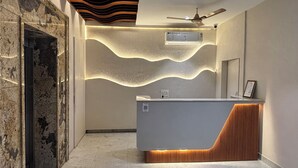 A modern reception area with a marble floor, a reception desk with a wooden accent, a ceiling fan, and an air conditioning unit. - Hotel Shree Rajasthan Inn (Ajmer)