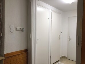Een gang met witte dubbele deuren, een houten bankje en een lichtschakelaar aan de muur.