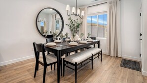 Un espace repas comprenant une table en bois foncé, six chaises, un banc, un grand miroir rond et un luminaire suspendu.