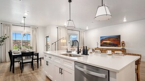 Une cuisine moderne dotée d’un grand îlot central, d’appareils électroménagers en acier inoxydable et de luminaires suspendus.