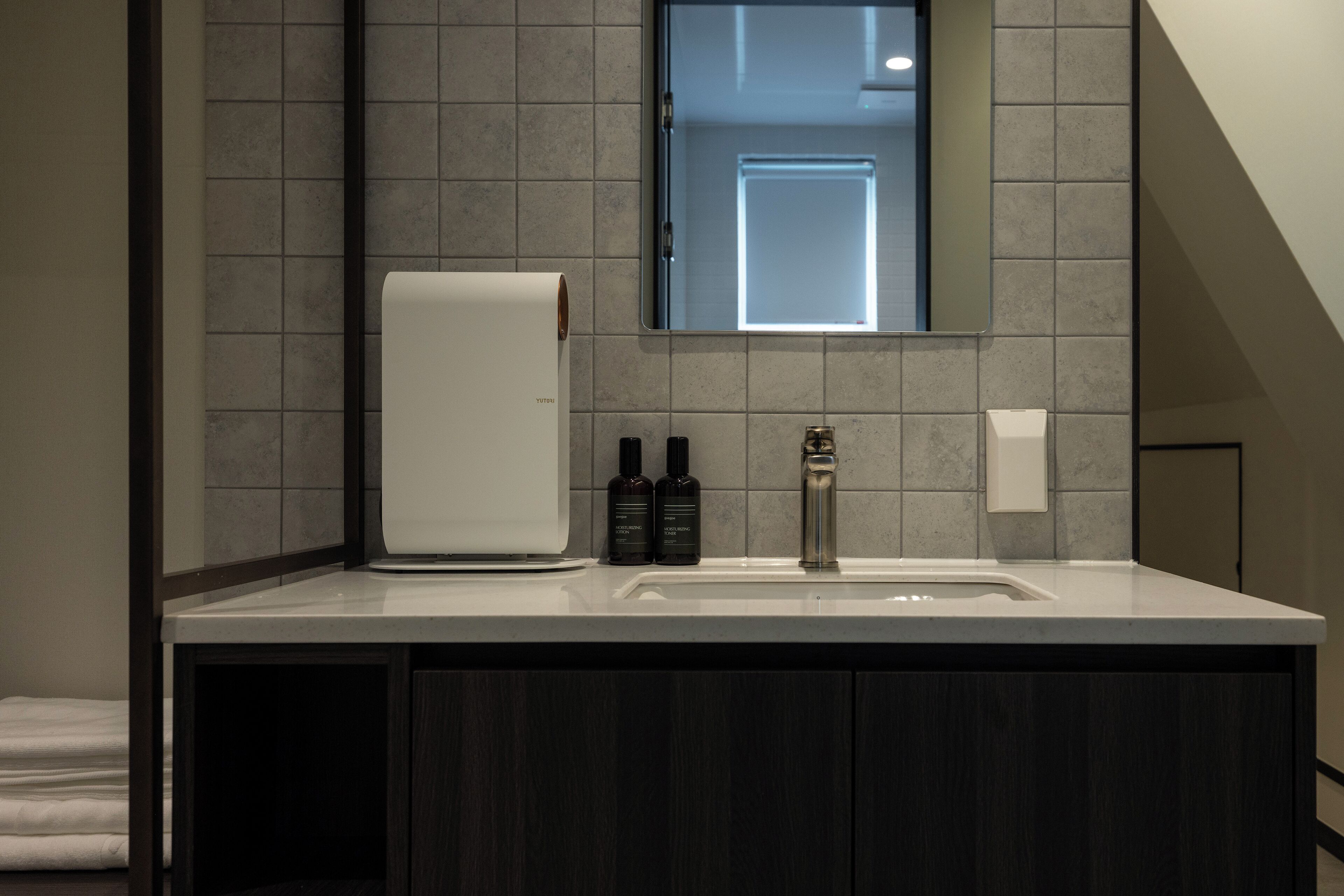 Un baño moderno con un lavamanos blanco, armarios de madera oscura y un espejo sobre el lavamanos.