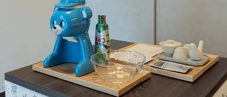 Un electrodoméstico azul sobre una bandeja de madera, un bol de vidrio, una botella y una bandeja con recipientes.
