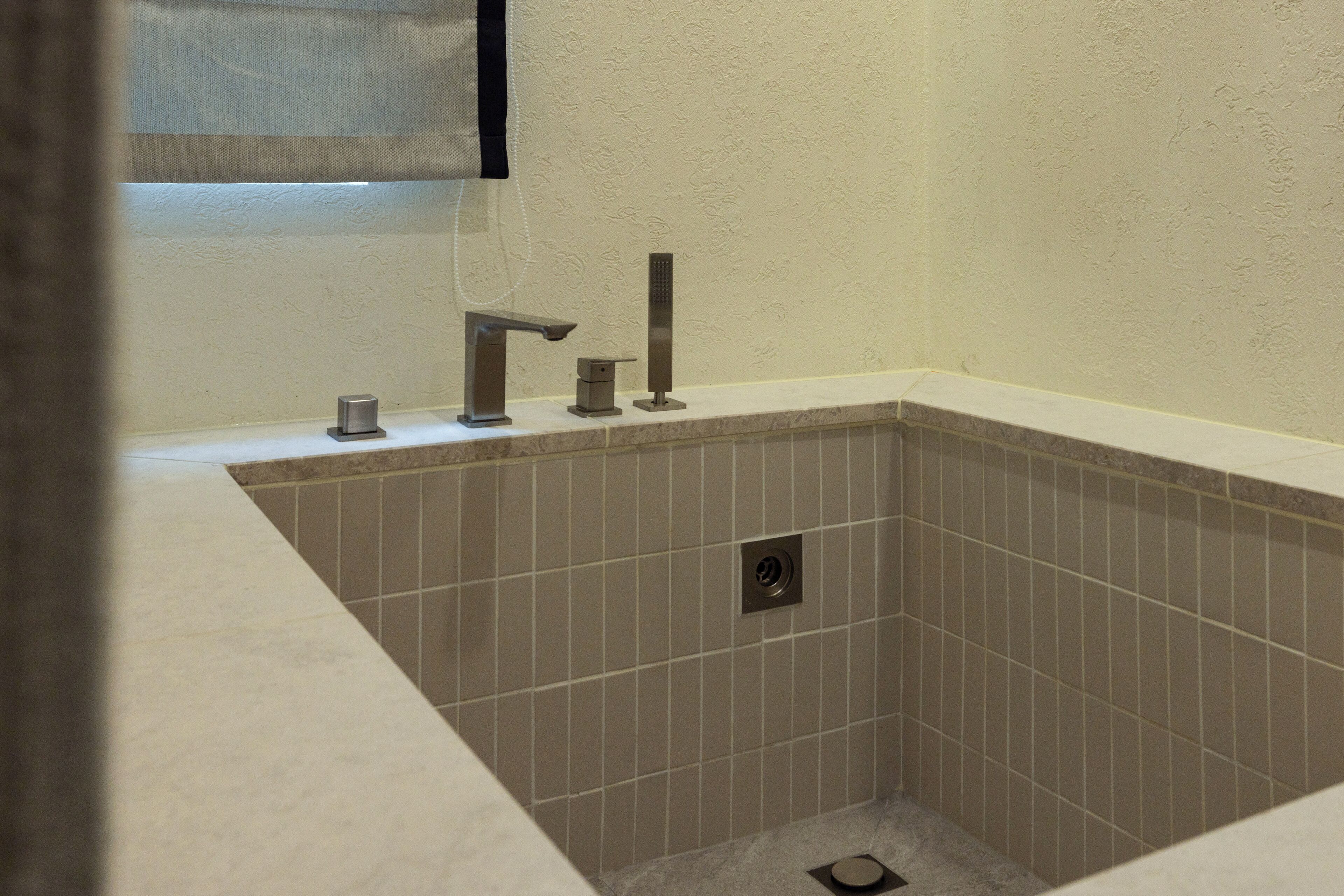 Un baño con una bañera rectangular, un cabezal de ducha manual y un grifo de pared.