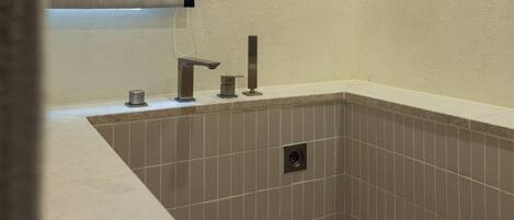 A bathroom with a rectangular tub, a handheld showerhead, and a wall-mounted faucet.
