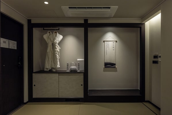 Ein Hotelzimmer mit einem dunkelholzigen Kleiderschrank, einem Bademantel, der an der Tür hängt, und einer kleinen Ablage mit Spiegel und Handtuch.
