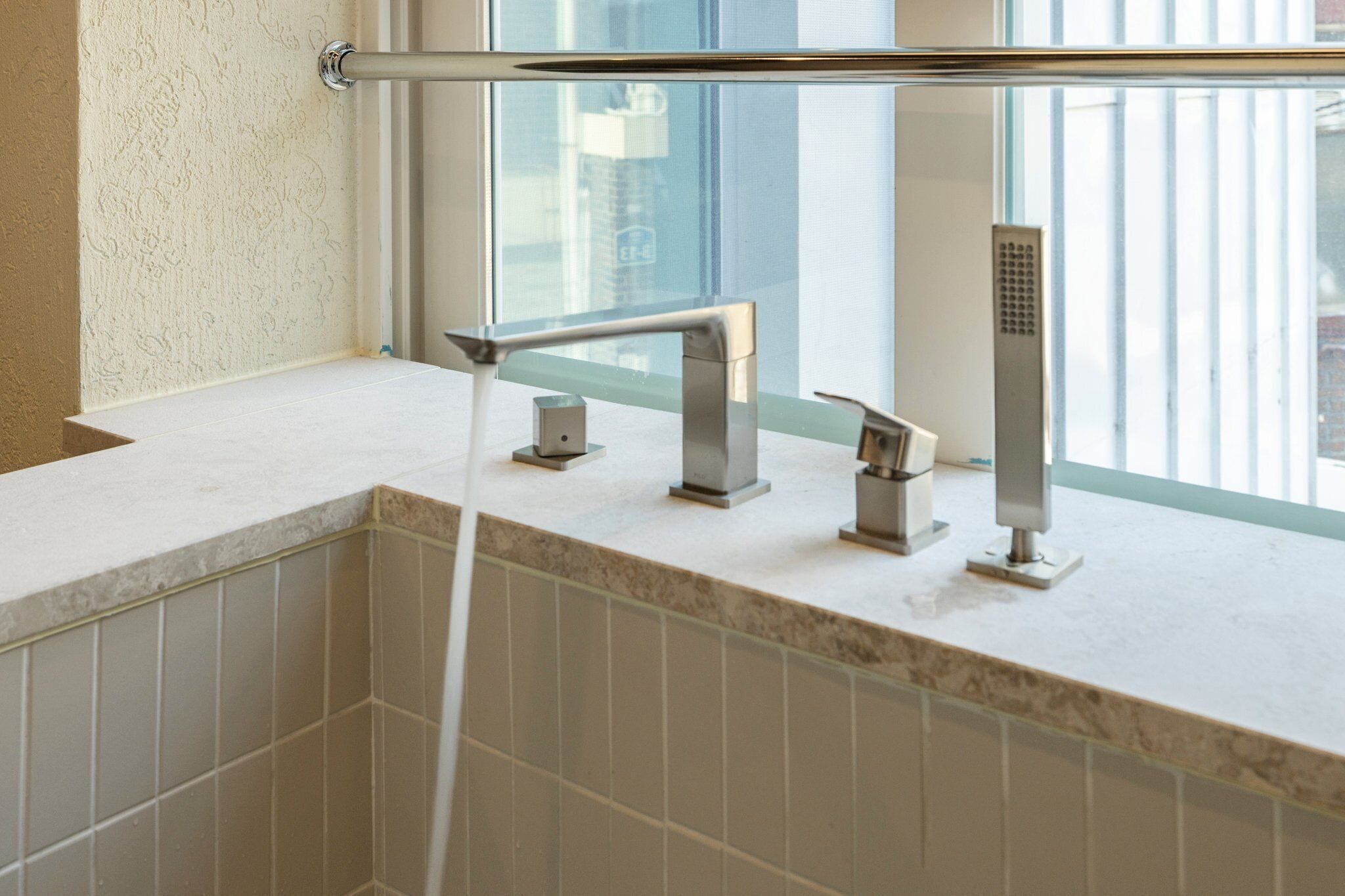 A bathroom with a white tiled wall, a window with a view of buildings, and a modern faucet.