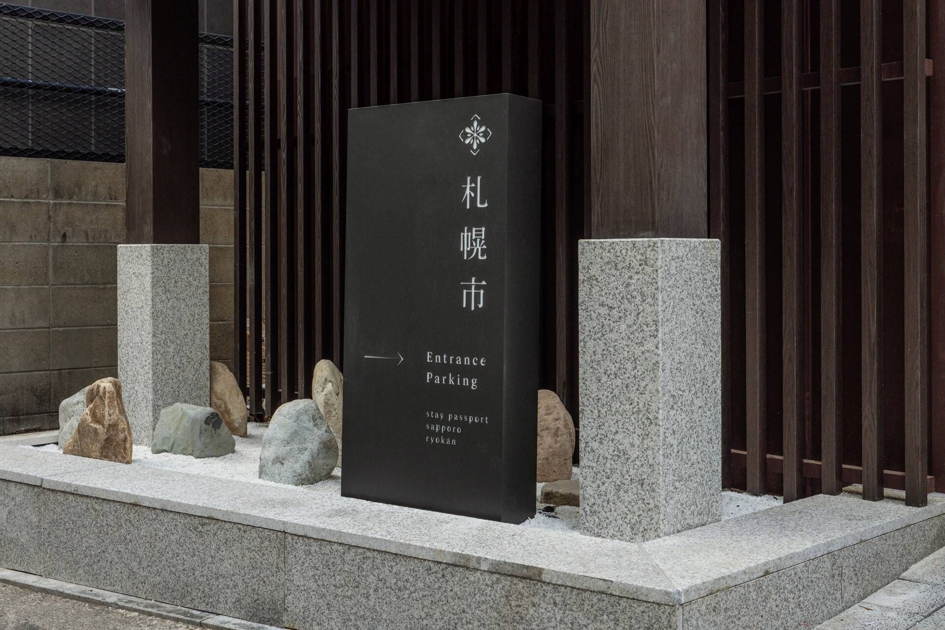 Un panneau noir avec du texte blanc indiquant « Entrée du parking » et donnant les instructions suivantes : « Conserver son passeport » et « Sapporo Ryokan ».