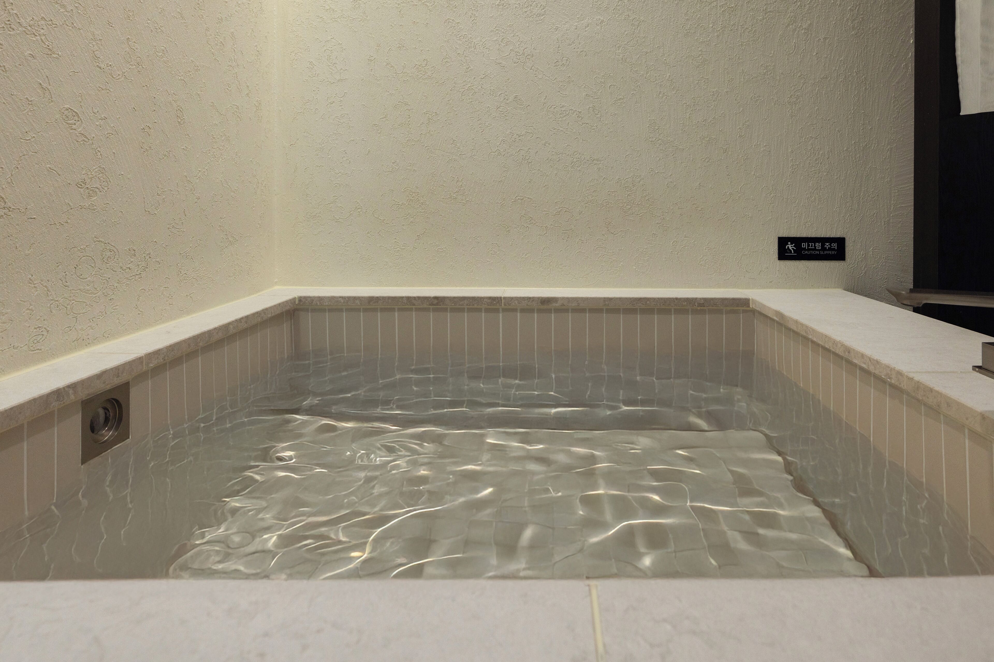 A hot tub with clear water, a tiled wall, and a caution sign.