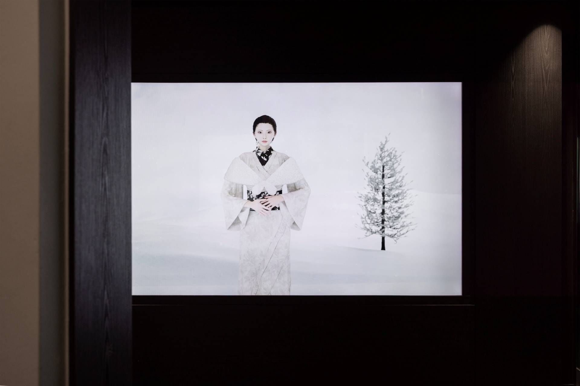 A person in traditional attire standing in front of a projection screen displaying a snowy landscape with a tree.