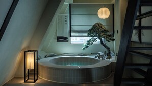 Une salle de bain moderne avec une baignoire sur pieds, un luminaire suspendu et un bonsaï.