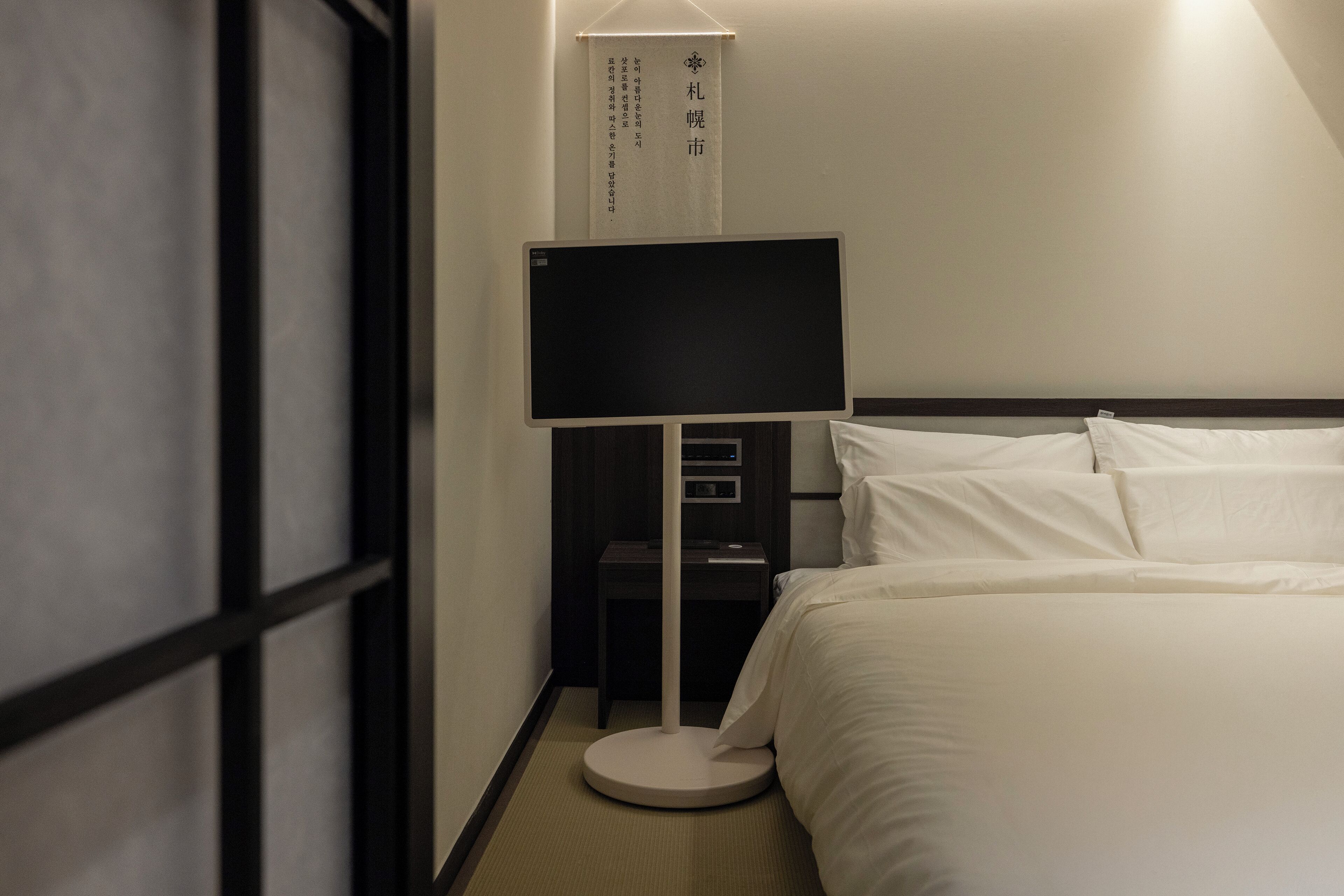 Ett hotellrum med en säng, ett sängbord, en platt-TV och en skylt som är upphängd på väggen.