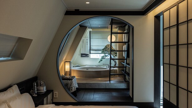 Une chambre avec un grand lit, donnant sur une salle de bain équipée d’une baignoire, et une porte coulissante qui mène à un balcon.