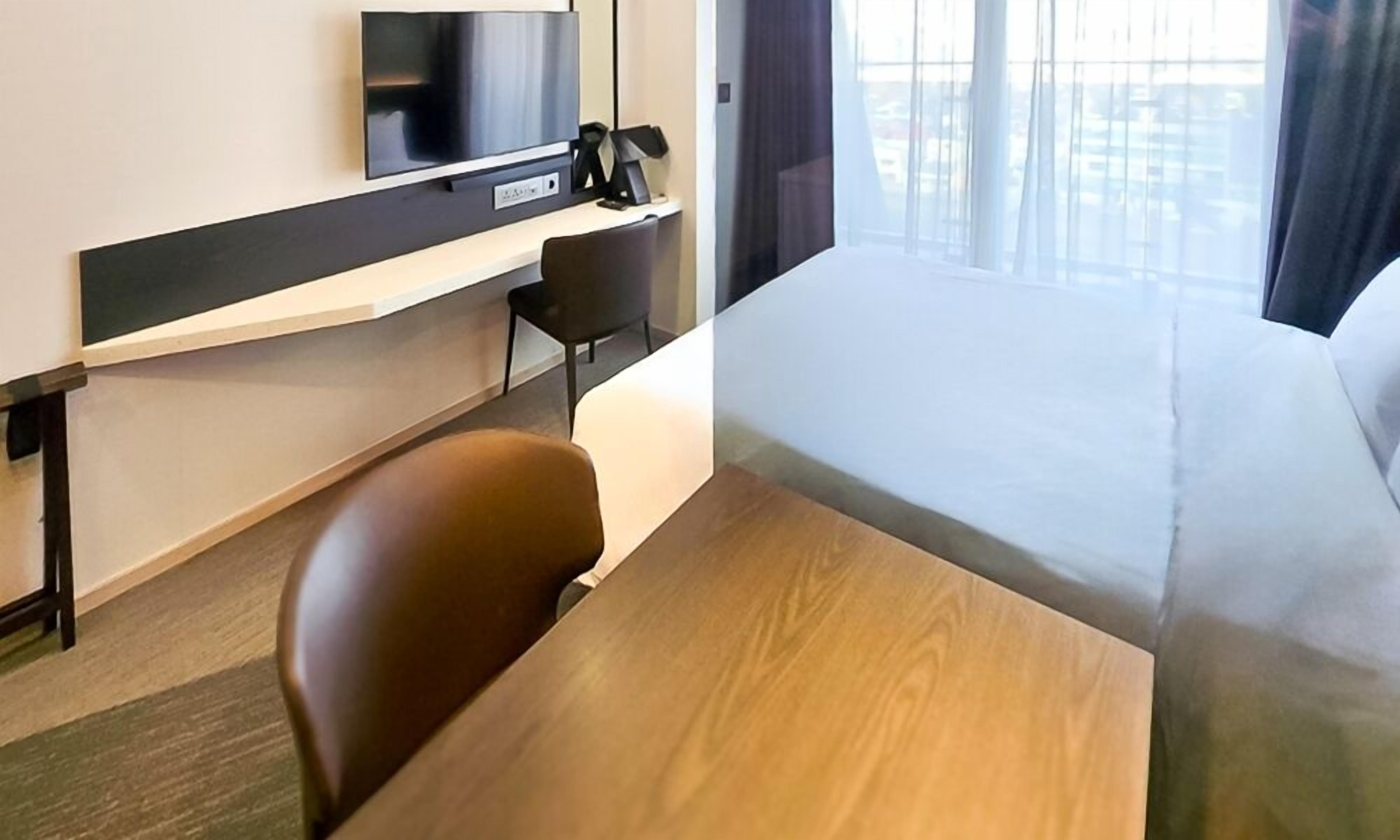 A hotel room with a bed, a desk, a chair, a television, and a window with curtains.