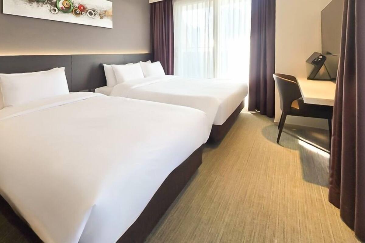 A hotel room with two beds, a desk, and a chair.