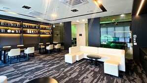 Un espace lounge moderne avec un tapis à motifs noir et blanc, des canapés blancs et un coin bar agrémenté d’étagères remplies de livres et d’objets décoratifs.