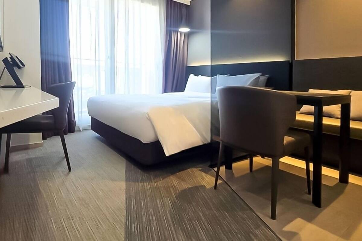 A hotel room with a bed, a desk, a chair, and a sofa.