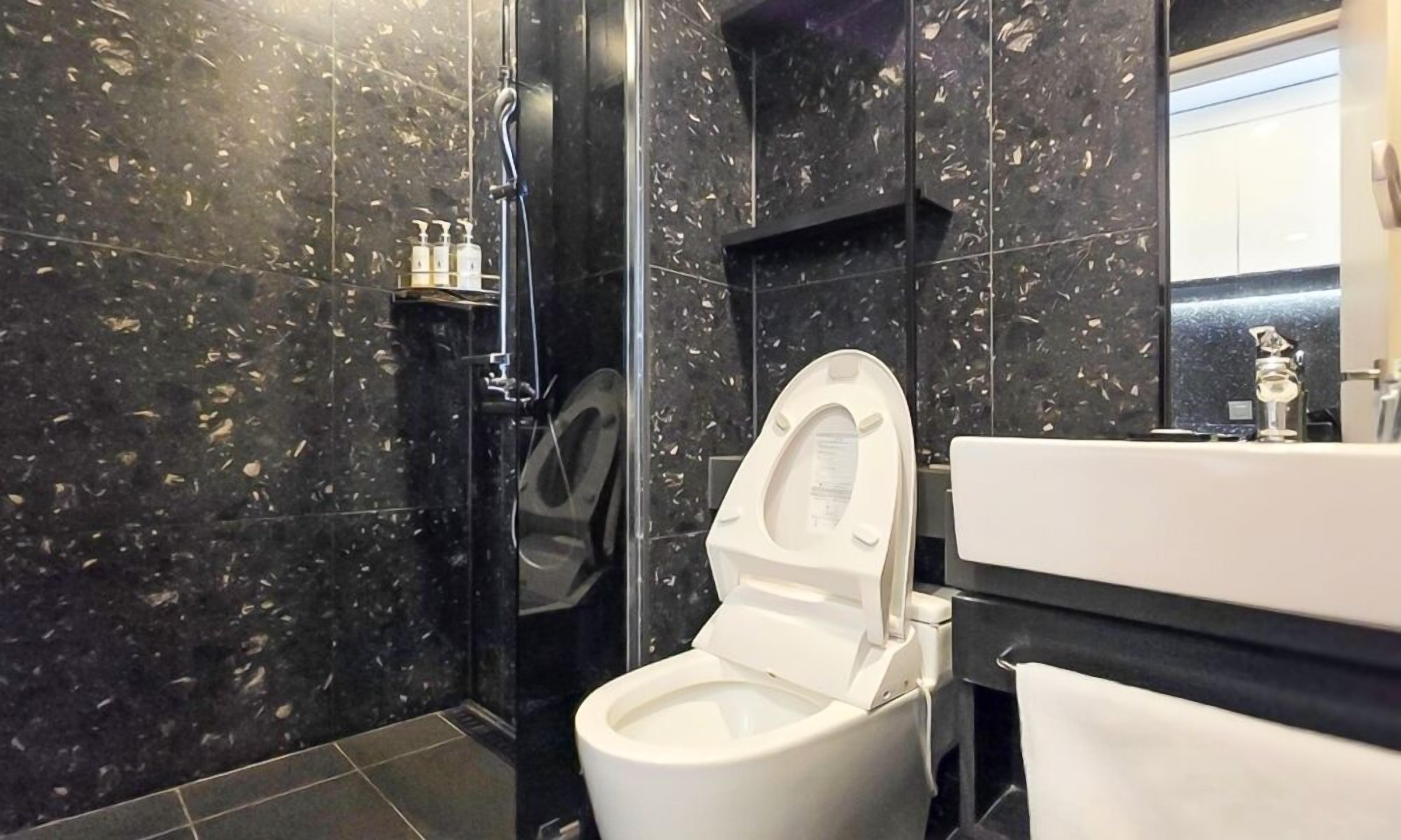 Un baño moderno con inodoro blanco, zona de ducha e lavabo.