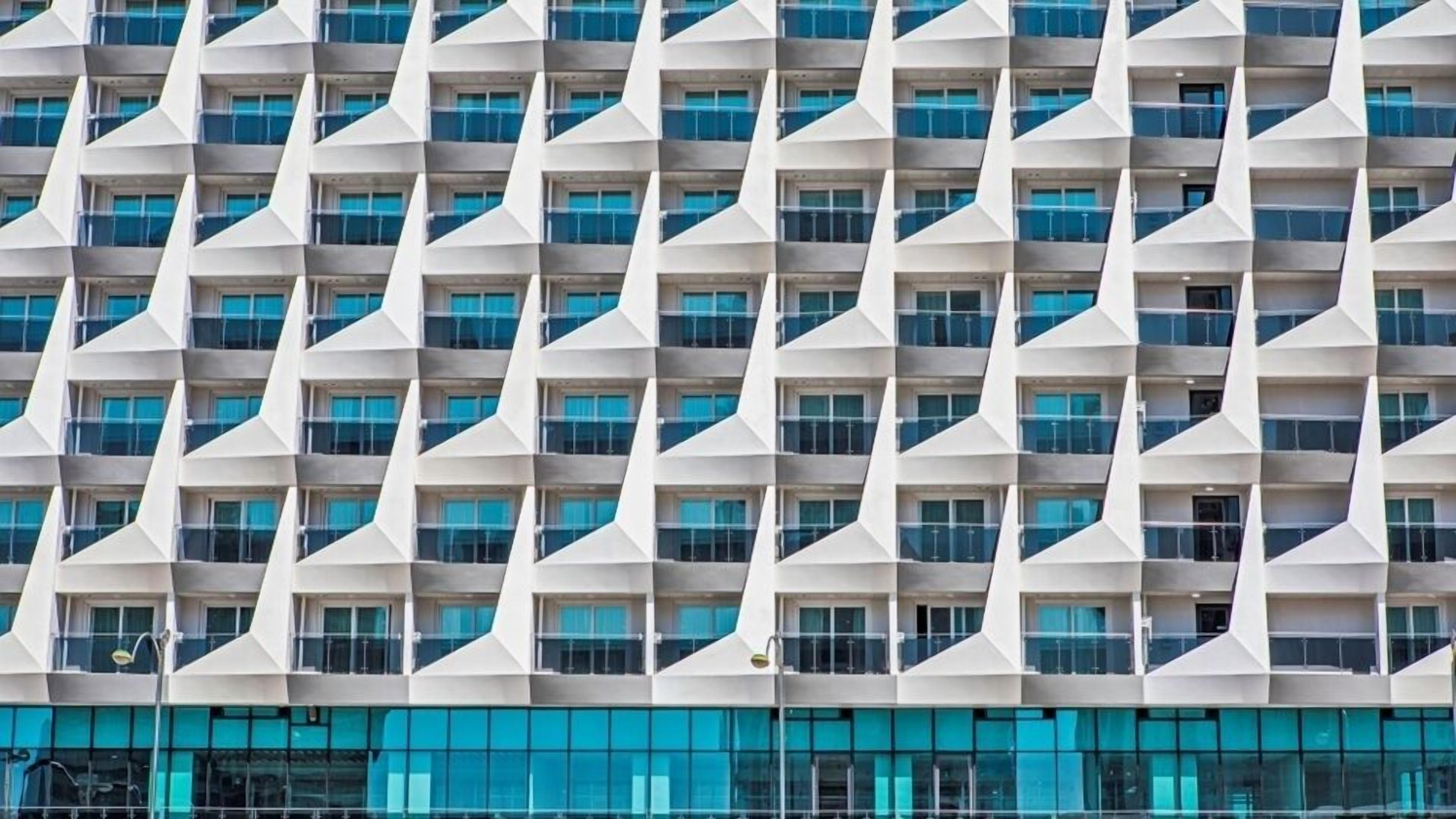 Um edifício moderno com fachada geométrica, apresentando padrões triangulares e uma série de janelas.